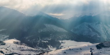 Kışın Dağları'nın muhteşem panorama. güneş ışığı ile bulutlu gökyüzü ile karlı tepeleri yaktı. küçük köy uzak Vadisi
