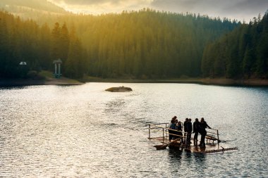 Synevir, Ukrayna - 20 Ekim 2008: bir gölün ortasında ahşap bir sal üzerinde genç turist grup. muhteşem akşam ışık uzaktan tepe üzerinde orman yukarıda. harika bir atmosfere sahip sonbahar