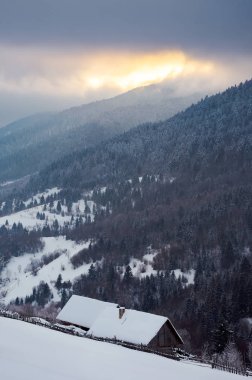 Odunluk kar karlı bir yamaç üzerinde örtülü. Harika kış manzara dağ sırtı yukarıda bulutlu gökyüzü ile. güzel doğa geçmiş gündoğumu vasıl