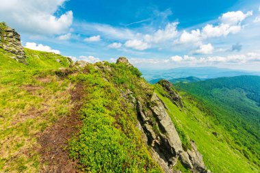 çimenli bir tepenin kayalık kenarına. dağ sırtı uzakta. Harika yaz hava. yumuşacık bulutların üstünde mavi gökyüzü