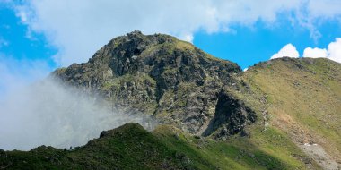 Bulutların arasındaki yüksek dağ zirveleri. Tepelerde karla kaplı harika bir yaz manzarası. Mavi gökyüzü bulutlu