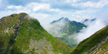 Bulutların arasındaki yüksek dağ zirveleri. Tepelerde karla kaplı harika bir yaz manzarası. Mavi gökyüzü bulutlu
