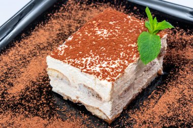 Siyah tabakta tarçınlı geleneksel zengin tiramisu keki. Naneli İtalyan tatlısı.