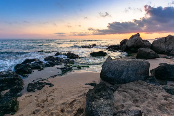 dramatic sunset on the ocean shore. waves crashing rocks on sandy beach. beautiful cloudscape above the horizon