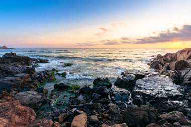 Gün batımında deniz kıyısında. Suda taşlar olan harika bir manzara. Güneş ve ufukta güzel bulutlar. Zen ruh hali ve maneviyat kavramı