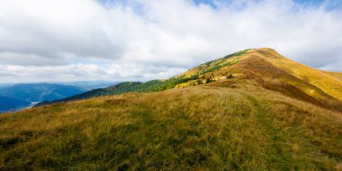 Sonbaharda yıpranmış çimlerde çayırlık alp. Dağlardaki güzel doğa manzarası. Uzakta dik bir zirve. Ufukta tepe var. Bulutlu gökyüzü ile benekli ışıkta renkli manzara