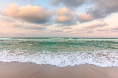 Bulutlu deniz manzarası. Kumsalda dalgalar var. Akşam ışığında rüzgarlı hava değişiyor.