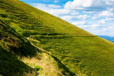 Travers dağ sırası boyunca ilerliyor. Tepelerdeki çimenler ve dik yamaçlar. Güneşli bir günde yaz manzarası. 