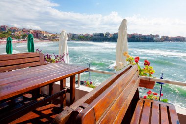 Denizdeki bir restoranın boş terası. Sabah ışığında körfeze güzel bir manzara. Ahşap masa ve koltukların üzerinde dekoratif şemsiye. güneşli hava