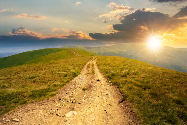 mountain road through grassy meadow at sunset. wonderful autumn adventure in evening light. clouds on the blue sky