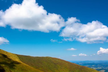Mavi gökyüzünün altında bulutlu tepeler ve çayırlar. Mavi gökyüzünün altında bulutlu tepeler ve çayırlar. Yazın sonlarında güneşli bir günde dağ manzarası. Ağustosta güzel bir manzara.