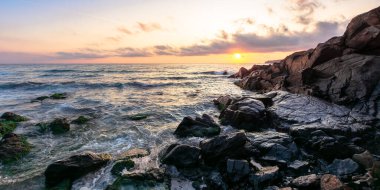 Gün batımında deniz kıyısında. Suda taşlar olan harika bir manzara. Güneş ve ufukta güzel bulutlar. Zen ruh hali ve maneviyat kavramı