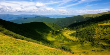 Yaz dağlarının tepeleri ve vadisi. Mavi gökyüzünde bulutlu güneşli bir hava. Benekli ışıkta güzel bir kornohora tepesi manzarası.