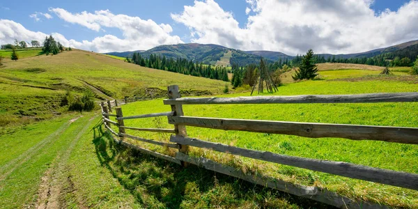 fence on the hill in rural area. early autumn scenery in carpathian mountains. sunny weather with clouds on the sky. hills rolling in tho the distant mountain ridge
