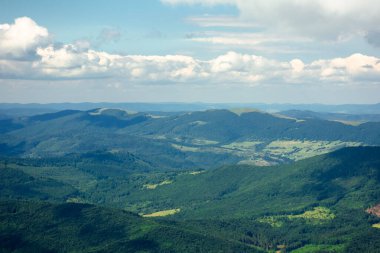 Bir yaz gününde dağ manzarası. Tepeler vadiden uzak tepeye doğru yuvarlanıyor. Bulutlu bir gökyüzünün altındaki muhteşem manzaranın manzarası