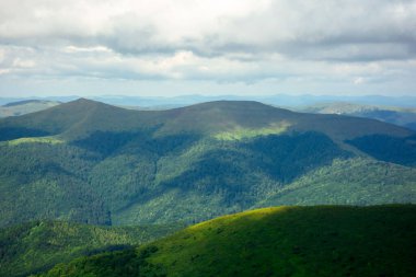 Bir yaz gününde dağ manzarası. Tepeler vadiden uzak tepeye doğru yuvarlanıyor. Bulutlu bir gökyüzünün altındaki muhteşem manzaranın manzarası