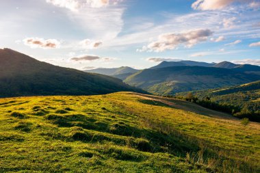 Gün batımında dağlarda kırsal alan. Akşam ışığında tepede çimenli bir çayır. Uzaktaki yüksek dağlar. Mavi gökyüzünde güzel bulutlar. harika erken sonbahar manzarası