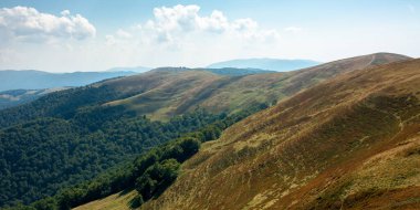 Güneşli bir sonbahar gününde dağ çayırı. Tepedeki kuru otlar. Dağ sırası ufka doğru ilerliyor. Mavi gökyüzünde öğleden sonra kabarık bulutlar