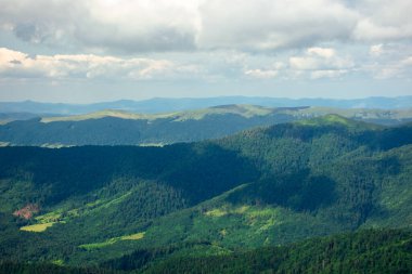 Bir yaz gününde dağ manzarası. Tepeler vadiden uzak tepeye doğru yuvarlanıyor. Bulutlu bir gökyüzünün altındaki muhteşem manzaranın manzarası