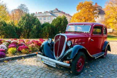 Uzhhorod, Ukrayna - 31 Ocak 2021: Izgarasında krom logosu olan kırmızı fiat 508 eski zamanlayıcı. Naroodna Meydanı 'ndaki sonbahar parkında güneşli bir hava. Sarı yapraklar ve çiçek tarlaları.