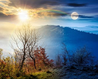 Dağdan sisli vadiye kadar bir manzara. Gündüz ve gece zaman kavramını değiştirir. Güzel sonbahar ekinoksu. Alacakaranlıkta güneşli ve aylı ormanlık tepeler. resimli dağlık kırsal alan manzarası