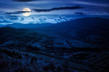 Geceleri dağlarda sonbahar manzarası. Kırsal manzara çok güzel. Arka planda renkli alpler var. Bulutlu gökyüzü. Dolunay ışığında vadide köyü olan kırsal bir manzara.