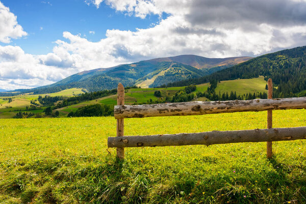 wooden fence on the grassy meadow in mountainous countryside. rural landscape of transcarpathia with rolling hill in september on a sunny day with clouds on the blue sky
