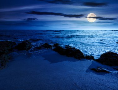 Kumsalda geceleri kum olur. Yaz tatilinde deniz kenarında. Dolunay ışığında sakin dalgalarla güzel bir deniz manzarası. Gökyüzünün altında kabarık bulutlarla deniz manzarası