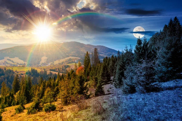 Sonbahar ekinoksunda çayırın arkasındaki kozalaklı ormanın manzarası. Gündüz ve gece zaman kavramını değiştirir. Mavi gökyüzü ve güneş ve ay ile kaplı dağ sırtı. Alp ormanları