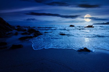 Sakin deniz manzarası. Geceleri kumlu sahilde dalgalanan kayalar. Dolunay ışığında manzaralı deniz manzarası. Rahatla ve yaz tatilinde kıyı konseptini düşün.