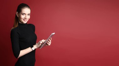 Tablet kullanma kırmızı bir arka plan üzerinde siyah elbiseli güzel bir gülümseyen beyaz kadın portresi