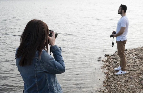 Woman photographer taking a picture of a man photographer in the bank of a lake