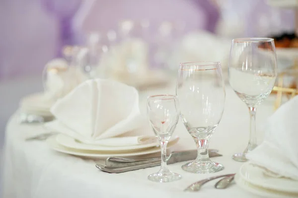 Three glass glasses of different sizes and shapes for cognac, for champagne, wine and drinks on a table covered with a white tablecloth, with white plates and a white cloth napkin