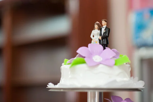 Wedding cake of white color and lilac flowers with figures of the groom and the bride close-up, the upper tier of the cake