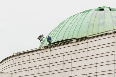 İki kişi yüksek bir binanın çatı onarımı