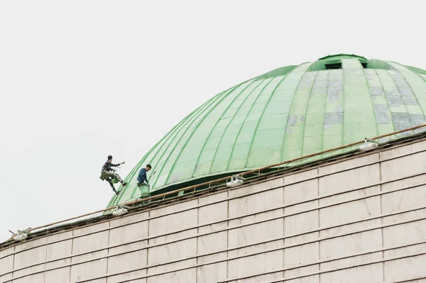 İki kişi yüksek bir binanın çatı onarımı