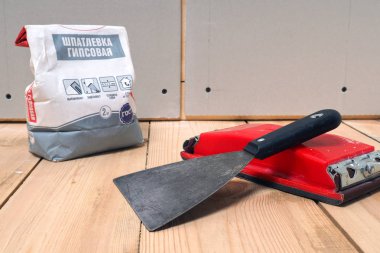 Macun, macun bıçak ve zımpara rende bir torba yerde vardır. Arkasında bir duvar drywall yaprak var. Ahşap tahta zemin