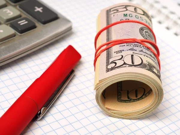 Coiling stack of dollars lies near the calculator. Close-up