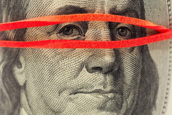 100 dolarlık banknot çok yakın. Franklin 'in yüzü maske gibi lastik bir bantla kaplı. Para masanın altında.
