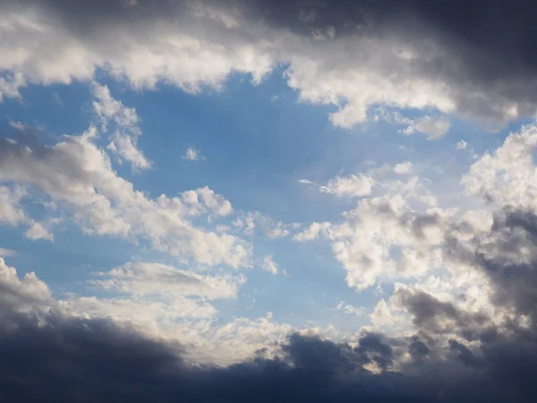 Blue sky and white clouds framed by dark thunderclouds after a storm. Dramatic spectacular backdrop or wallpaper. Bright prospect and desire to move towards a goal through difficulties and hardships