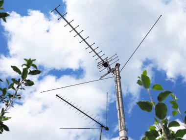 Açık hava televizyon antenleri gökyüzü ve bulutların arka planına karşı derme çatma direklerde duruyor. Yazın kırsal kesimde çekilmiş. Televizyon ve medya teması üzerine parlak illüstrasyon