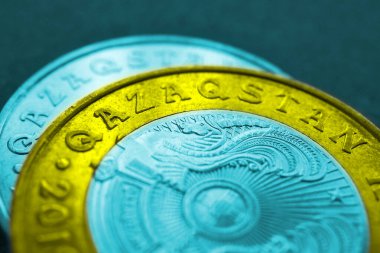 Yazıtın çevirisi: Kazakistan. Kazak sikkelerinde 100 ve 50 tenge içerisindeki ülkenin adı. İllüstrasyon, ulusal bayrağın renkleriyle renklendirilmiştir. Latin alfabesine geçiş. Makro