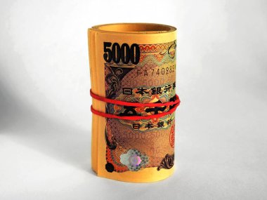 Bir deste Japon 5000 yenlik banknot beyaz bir kağıdın üzerinde duruyor. Notlar sarılı ve elastik bir bantla bağlanmış. Finansal bir tema üzerine dramatik koyu renkli illüstrasyon. Makro
