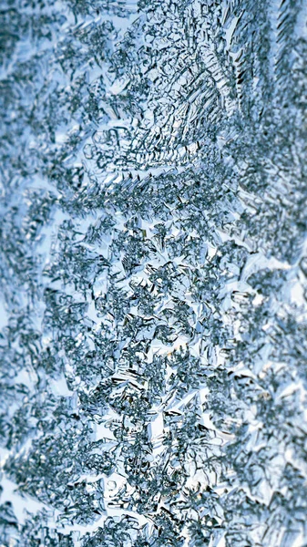 A pattern of ice crystals close-up on a window glass in winter. Vertical light blue and white background or wallpaper. Frozen water. Weather forecast: frost, cold snap. Strong macro