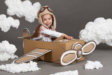 karton kutu ve bir pilot olma hayalleri bulutlar Pamuk yün gri bir arka plan üzerine yapılmış bir uçak kız çocuk oynar