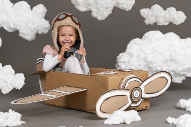 karton kutu ve bir pilot olma hayalleri bulutlar Pamuk yün gri bir arka plan üzerine yapılmış bir uçak kız çocuk oynar