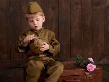 Çocuk Çocuk giymiş retro askeri üniformalı asker olarak oturan eski bavul, koyu ahşap arka plan, retro tarzı şişesi ile