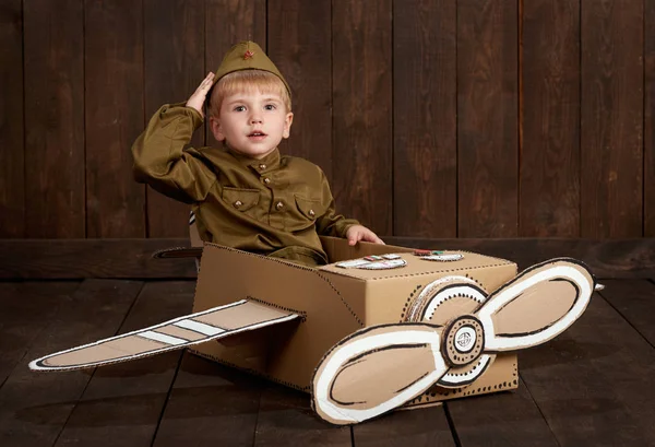 çocuk çocuk asker retro askeri üniformaları Sit karton kutu ve bir pilot, koyu ahşap arka plan, retro tarzı olma hayalleri yapılmış bir uçak olarak giyinmiş