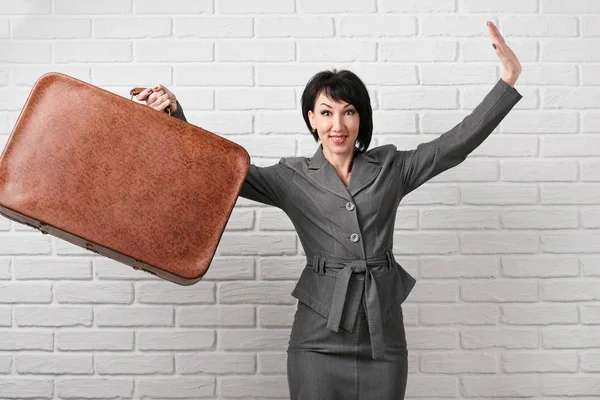 business woman dressed in a gray suit with suitcase stay in front of a white wall
