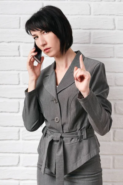 business woman dressed in a gray suit talking on the phone, stay in front of a white wall